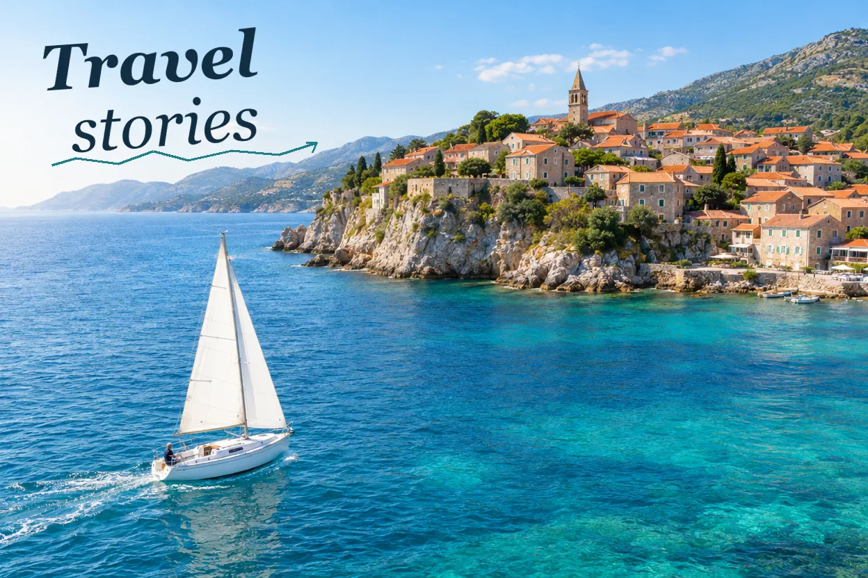 white sailboat; turquoise sea; terracotta coastal village; establishing view. Artwork lettering: Travel stories